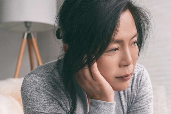 Adrenal-Fatigue-Doctor A middle-aged asian woman sitting on her couch, resting her head on her hand, suffering from adrenal fatigue. Get treatment for adrenal fatigue syndrome from Stephen Beyer, DC in Mokena.