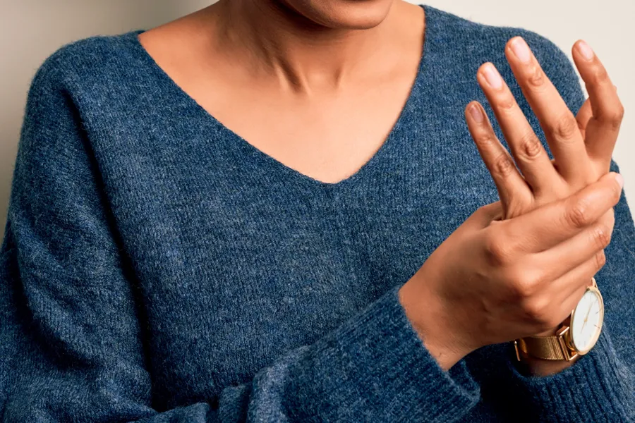 Arthritis-Doctor Close up of a woman in a blue sweater massaging one aching hand with the other. Get help for arthritis from Stephen Beyer, DC in Mokena.