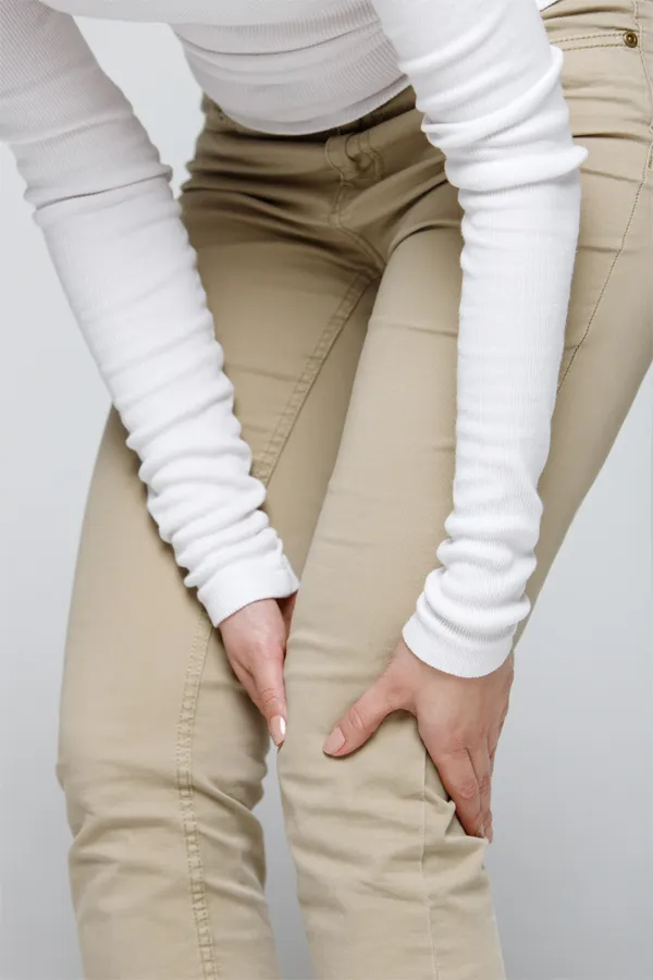 Arthritis-Treatment A woman wearing a white long-sleeve shirt and tan pants, clutching her knee, suffering from arthritis. Get arthritis treatment from Stephen Beyer, DC in Mokena.