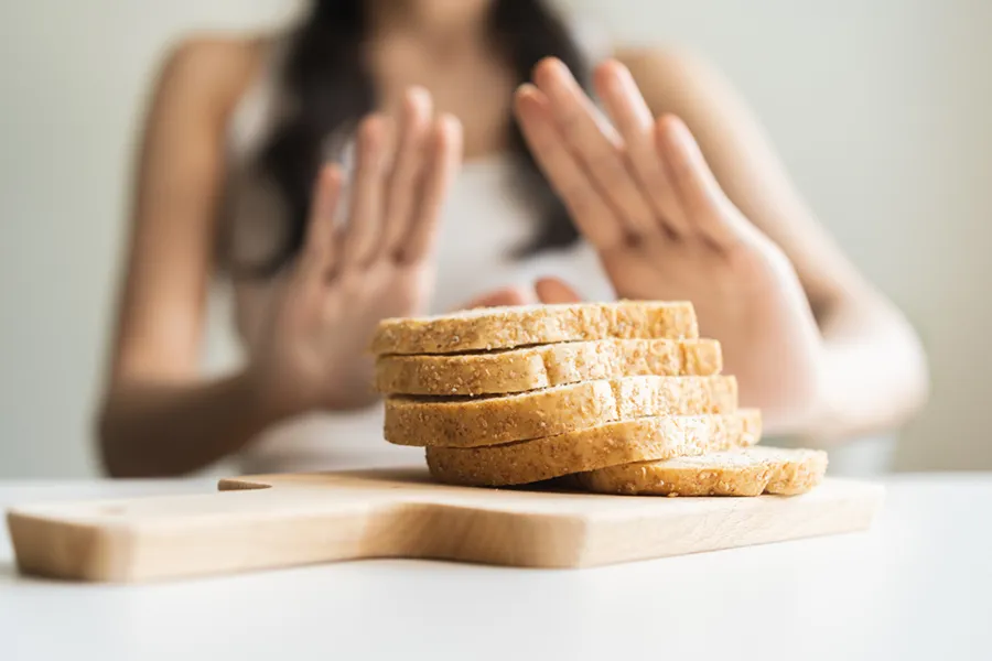 Celiac-Disease-Clinic Close up of a stack of bread slices on a cutting board with a woman's hands behind them, refusing to eat. Get treatment for Celiac Disease from Stephen Beyer, DC in Mokena.