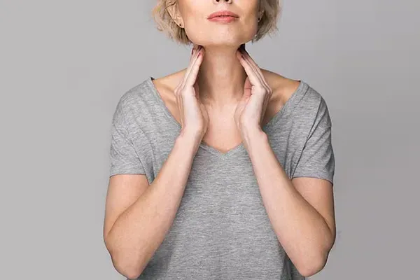 Hashimotos-Thyroiditis-Doctor An older blonde woman in a gray t-shirt holds her hands to her neck checking for signs of thyroid problems. Get help for Hashimoto's Thyroiditis from Stephen Beyer, DC in Mokena.