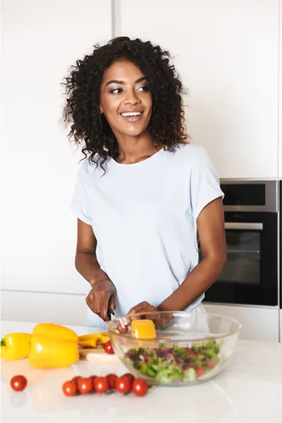 Irritable-Bowel-Syndrome-Treatment Image featuring a smiling woman chopping vegetables for a salad in a bright, white kitchen. Stephen Beyer, DC offers Irritable Bowel Syndrome Treatment and Digestive Support in Mokena.