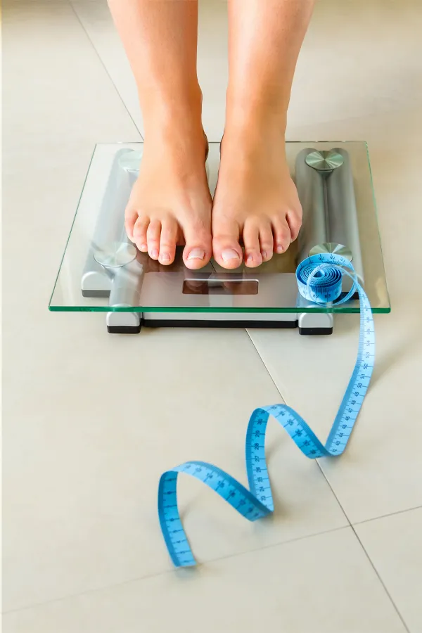 Weight-Loss-Resistance-Treatment Close-up of a woman's feet standing on a scale, with measuring tape by her toes, getting treatment for weight loss resistance from Stephen Beyer, DC in Mokena.